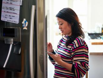 woman opening fridge checking phone