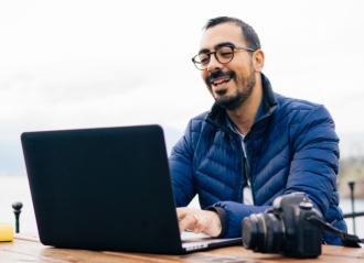 man outside working on laptop with DSLR camera on table